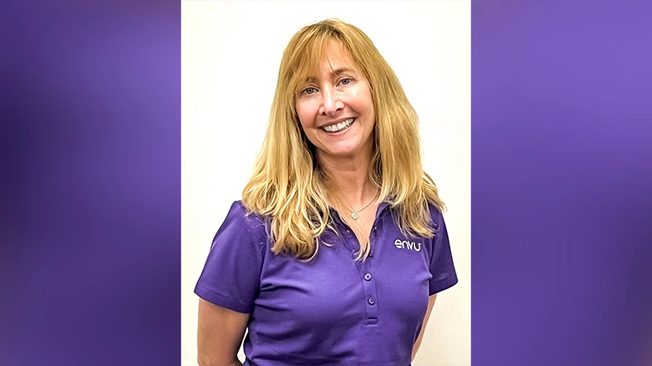 A smiling woman with long blonde hair wearing a purple polo shirt is visible from the waist up in this headshot photo.